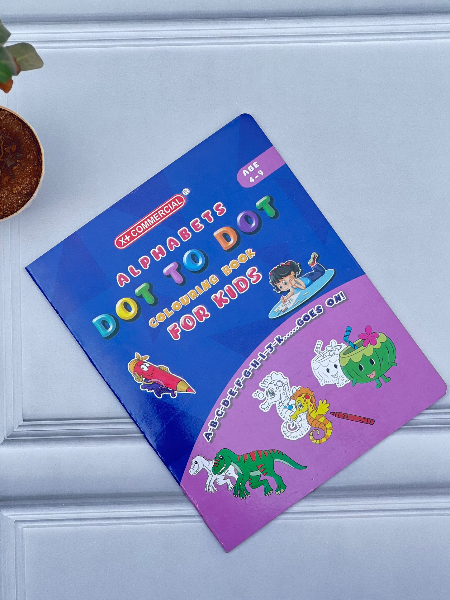 Colorful children's activity book on a white surface with a plant in the corner.